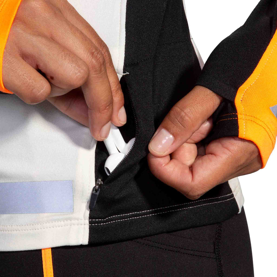 The zippered pocket on the left side of the Brooks Women's Run Visible 1/2 Zip 2.0 in the Ecru/Fluoro Flash/Black colourway.  (8499447333026)