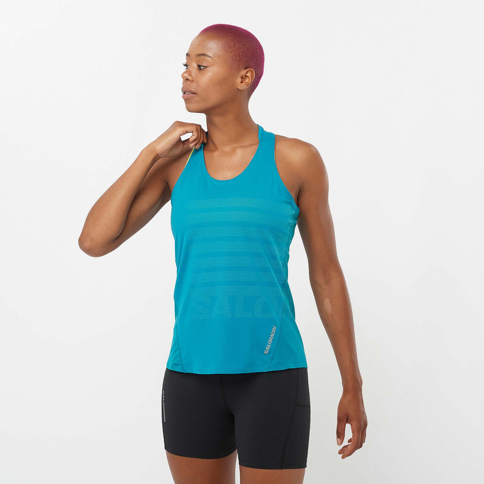 Front view of a model wearing a Salomon Women's Sense Aero GFX Singlet in the Tahitian Tide/Peacock Blue colourway. Model is also wearing Salomon running shorts. (8157872914594)