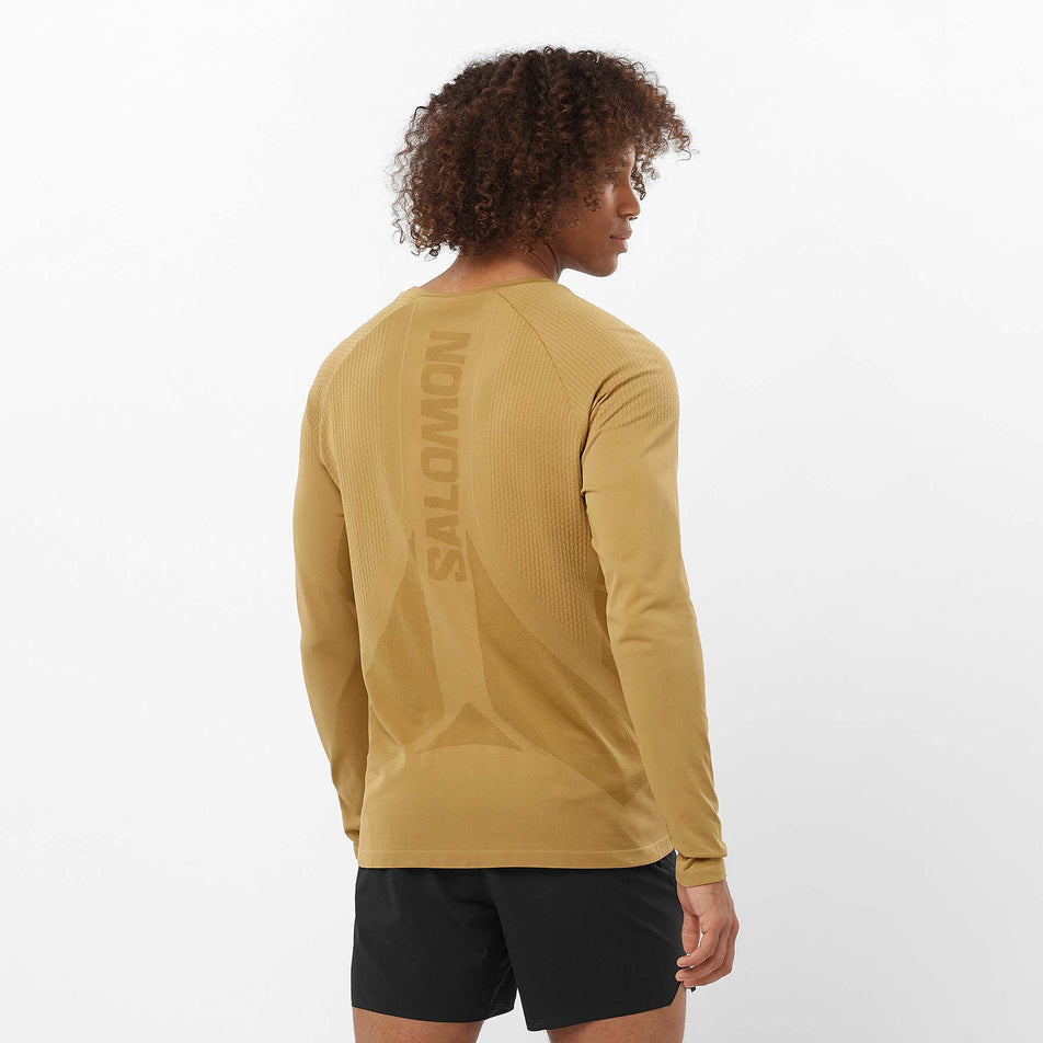 Back view of a model wearing the Salomon Men's Aero Seamless Long-Sleeve T-Shirt in the Antique Bronze colourway. Model is also wearing shorts. (8509564846242)