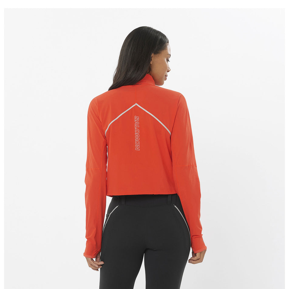Back view of a model wearing a Salomon Women's Sense Aero Hybrid Cropped Half Zip Midlayer in the Cherry Tomato colourway. Model is also wearing leggings. (8462927102114)