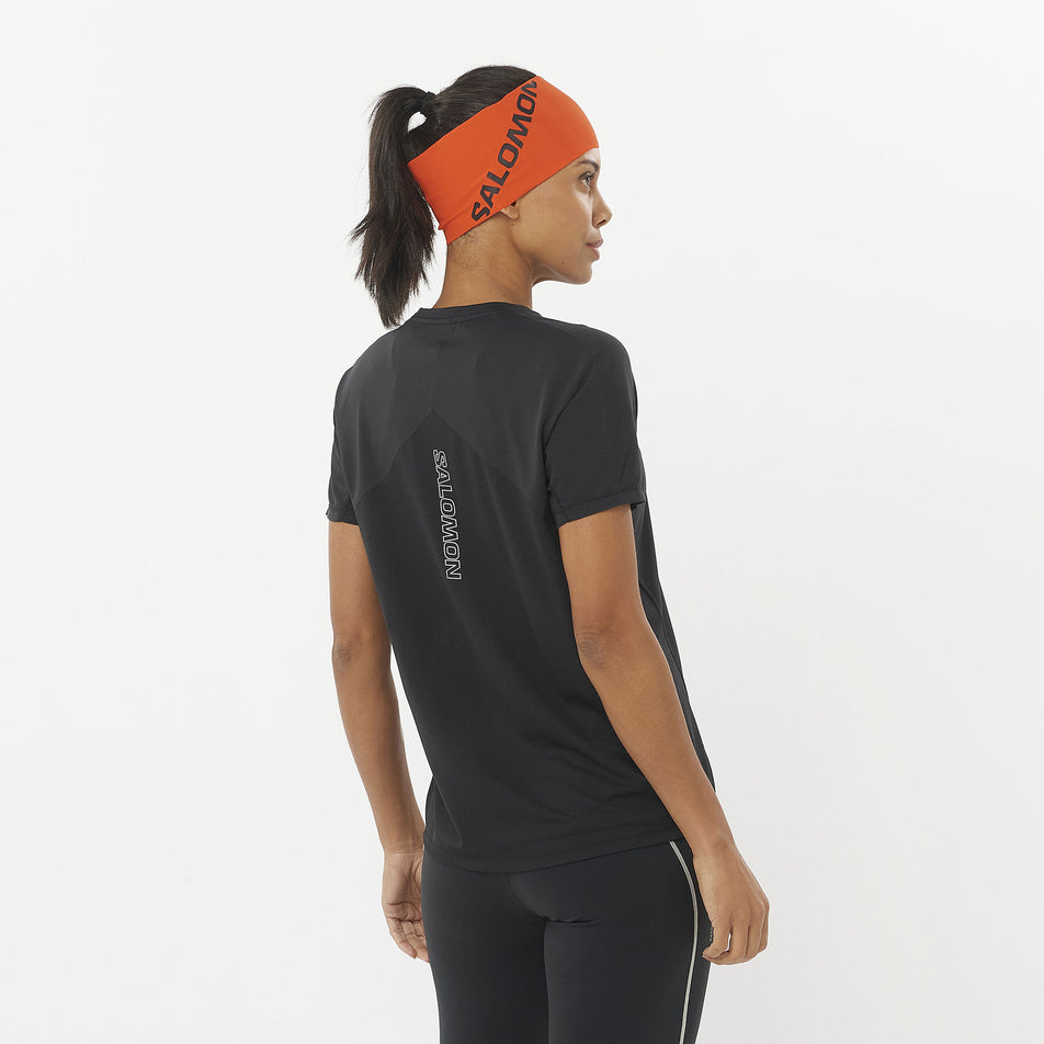Back view of a model wearing a Salomon Women's Sense Aero Short Sleeve T-Shirt in the Deep Black colourway. Model is also wearing leggings and a headband. (8462977695906)