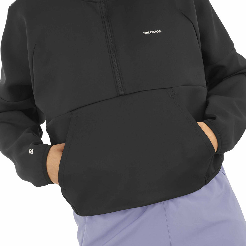 A model demonstrating the pockets on the front of the Salomon Women's SHKout Half Zip Midlayer in the Deep Black colourway. (8575544721570)