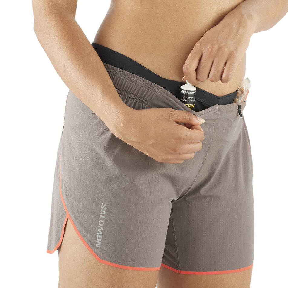 Front view of a model demonstrating that nutrition can be stored in the front stretch pocket on the waistband of a pair of  Salomon Women's Sense Aero 5