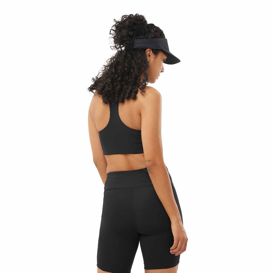 Back view of a model wearing the Salomon Women's SHKout CORE Sports Bra in the Deep Black colourway. (8574537859234)