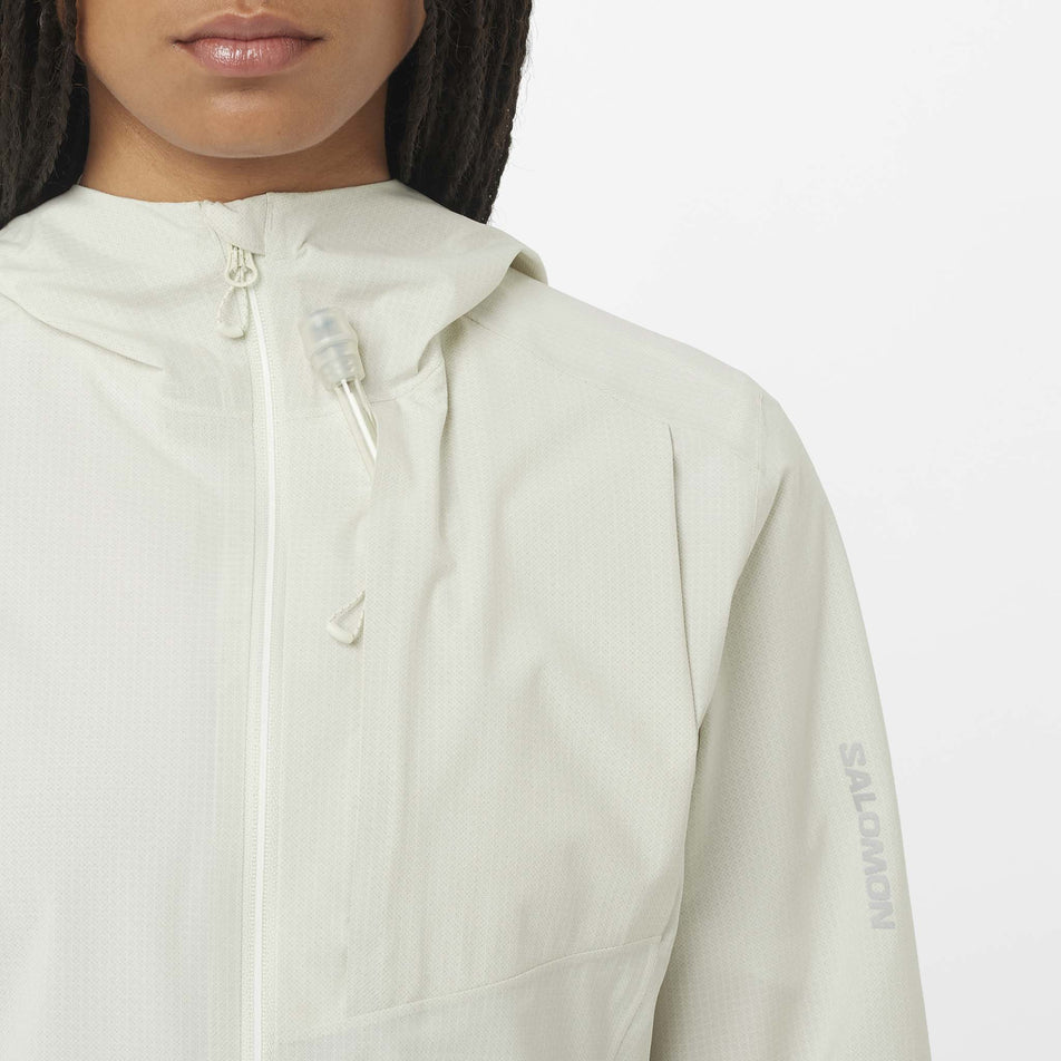Front view of a model wearing the Salomon Women's Bonatti Trail Shell Jacket in the Icicle colourway. Image shows the pipe and valve of a soft flask bottle coming through the chest pocket. (8576408846498)