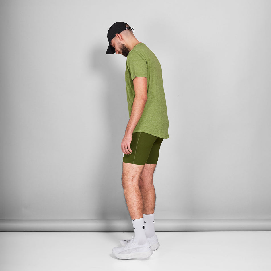Side view of a model wearing a SAYSKY Men's Logo Combat Pro T-Shirt in the Green Melange colourway. Model is also wearing shorts, socks, shoes, and a cap. (8644805755042)