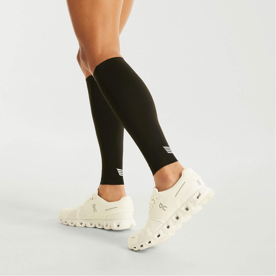 Side view of a model wearing the Pressio Unisex EQ Compression Calf Guards in the Black colourway. Model is also wearing shoes. (8475847393442)
