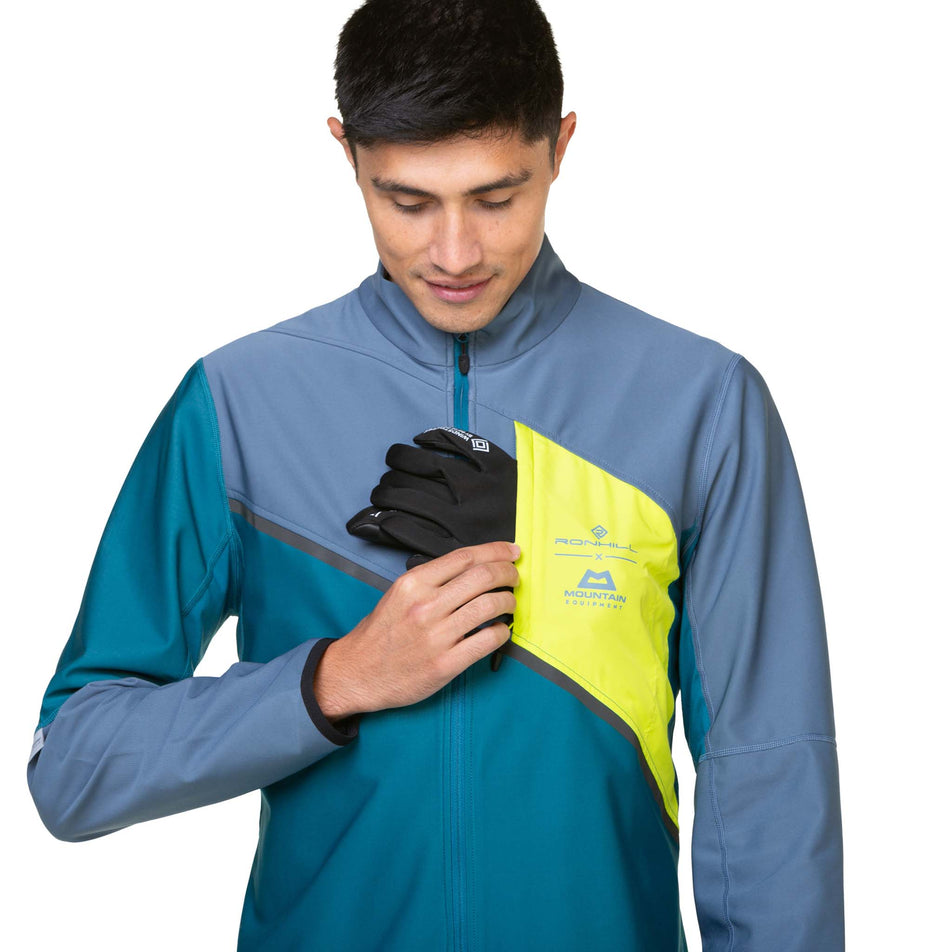 A model demonstrating that gloves can be stored in the chest pocket of a Ronhill Men's Tech GORE-TEX Windstopper Jacket in the Deep Teal/Lake Acid colourway. Jacket is being worn by a model.  (8470614016162)