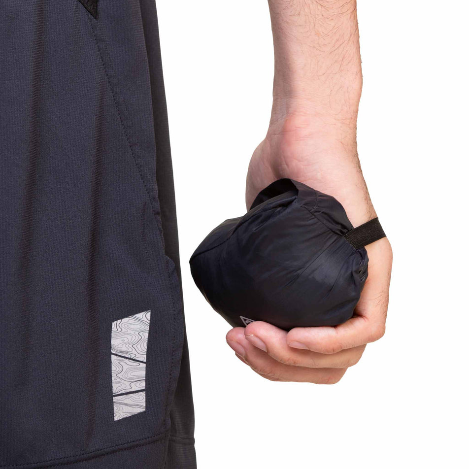 A model holding a Ronhill Men's Tech All-Terrain Jacket in the All Black colourway that has been folded up into the storage pocket. (8563617431714)