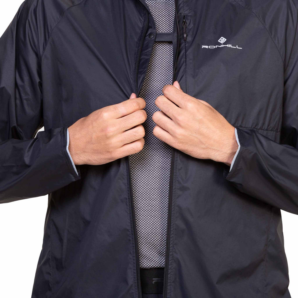 Front view of a model wearing the Ronhill Men's Tech All-Terrain Jacket in the All Black colourway with the chest clip fastened. (8563617431714)