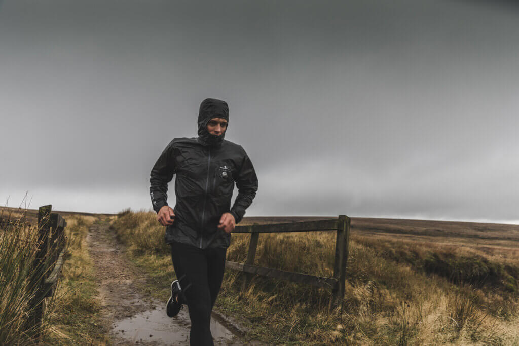 Man running along a trail in bad weather wearing a Ronhill x Mountain Equipment Tech Gore-Tex Jacket